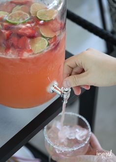 a person pours a drink into a glass with ice and strawberries in it