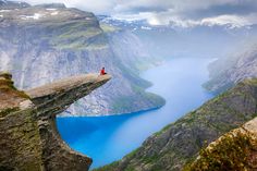 a person standing on the edge of a cliff overlooking a body of water and mountains