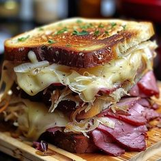 a sandwich with meat, cheese and onions on a cutting board next to a glass of beer