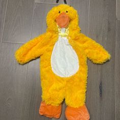 a yellow stuffed animal on the floor with an orange beak and white dress up shirt