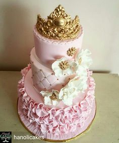 a three tiered cake with pink and gold frosting on the top, topped with flowers