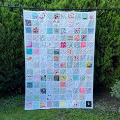 a quilt hanging on a fence in front of some bushes