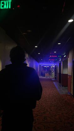 a person walking down a hallway at night with the exit sign lit up behind them