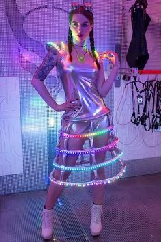 a woman in a silver dress with neon lights on her body and arms, posing for the camera