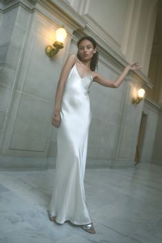 a woman in a long white dress standing on the floor with her hand out and looking off to the side