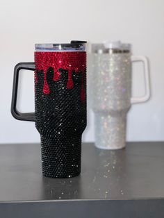 a black and red coffee cup sitting on top of a counter next to a white mug