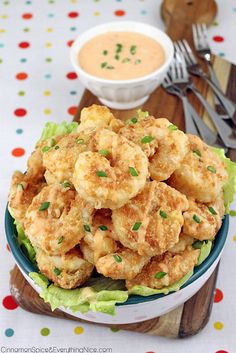 a bowl filled with fried shrimp on top of lettuce next to a fork and spoon