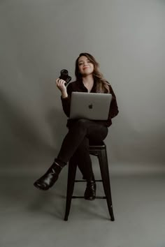 a woman sitting on a stool with a laptop computer in front of her, holding an object