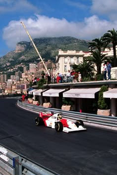 a man driving a race car down a street next to a tall building with a mountain in the background