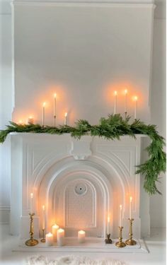 a mantel with candles and greenery on it in front of a white fireplace