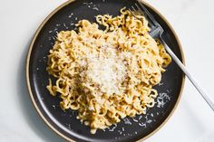 a black plate topped with pasta covered in parmesan cheese next to a fork