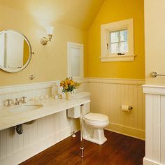 a white bathroom with yellow walls and wood flooring, along with two sinks on either side of the bathtub