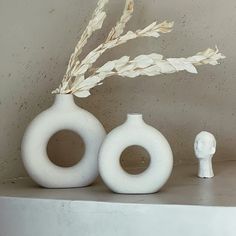 two white vases sitting on top of a shelf next to a small figurine