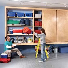 two people are working on the shelves in a room with blue walls and wooden cabinets