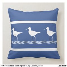 three seagulls are standing on the water in front of a blue pillow with white stripes