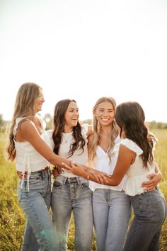 four young women standing in a field hugging each other