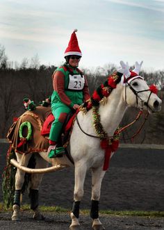 a man riding on the back of a white horse wearing a santa hat and christmas decorations