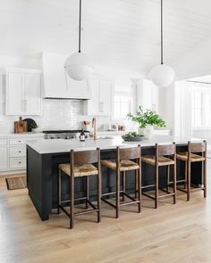 a large kitchen with white cabinets and black island countertops, wooden stools, and pendant lights