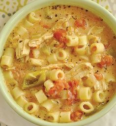 a green bowl filled with pasta soup on top of a white and yellow table cloth