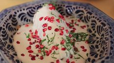 a blue and white bowl filled with food covered in pomegranate on top of a table