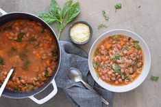 two bowls of beans and spinach soup on a table with spoons next to it