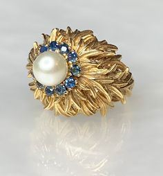 Vintage Pearl Ring, Pearl Gold Ring, Pearl Sapphire Ring, Pearl Ring For Women, Gold Leaf Ring, Vintage Leaf Ring, Vintage Gold Jewelry A fascinating collectors item. This solid 14k gold ring features a single pearl surrounded by a halo of blue sapphires set above an eye- catching pile of intertwined golden leaves. * Ring size: US 5 1/2 * Complimentary resizing is available up to 3 sizes larger or smaller than stated size. Elegant Multi-stone Cluster Ring Collectible, Elegant Yellow Gold Dome Ring For Collectors, Elegant Multi-stone Dome Ring For Anniversary, Yellow Gold Multi-stone Round Pearl Ring, Yellow Gold Multi-stone Pearl Ring, Anniversary Multi-stone Dome Ring In Fine Jewelry Style, Formal Yellow Gold Multi-stone Pearl Ring, Fine Jewelry Hallmarked Sapphire Open Ring, Fine Jewelry Sapphire Ring With 17 Jewels