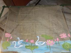 a piece of cloth with water lilies and swans painted on it, sitting in front of a window