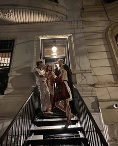 three people are standing on the stairs in front of a building at night, one person is taking a selfie