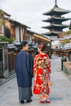 a man and woman dressed in traditional japanese garb walking down an alley way with pagodas in the background