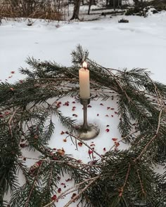 a candle is lit in the middle of a snowy circle with pine needles and berries