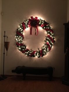 a christmas wreath is hanging on the wall next to a bench with lights around it