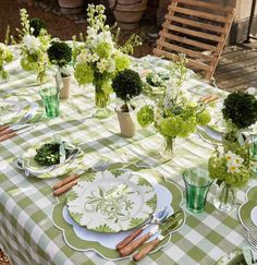 the table is set with green and white flowers in vases, plates and utensils