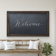 a welcome sign hanging on the wall next to a bench with pillows and a potted plant