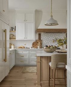 a kitchen with white cabinets and wood floors, an island countertop and two stools