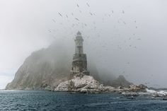 a lighthouse on an island in the middle of the ocean with seagulls flying around it