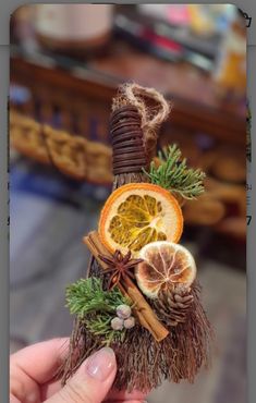 a person holding up a miniature orange and cinnamon stick with pine cones on it's end