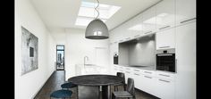 a modern kitchen with white cabinets and an oval dining table in the center, along with two blue bar stools