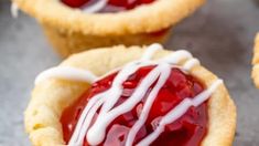 three small pastries with white icing and cherries on top, sitting next to each other