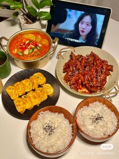 a table topped with plates of food and bowls of rice next to a laptop computer