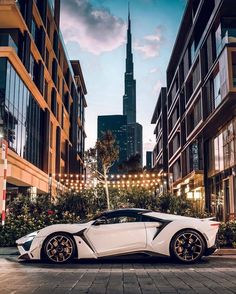 a white sports car parked in front of tall buildings on a city street at night