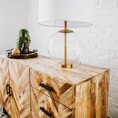 a lamp on top of a wooden dresser next to a white brick wall