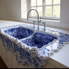 an ornate blue and white sink in a kitchen with tile countertops, windows, and cabinets