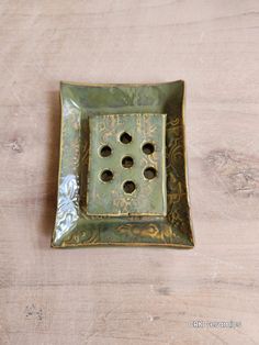 a green square dish with holes in the center on a wooden surface, resting on top of a table