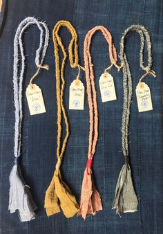 five scarves are laid out on a blue piece of cloth with tags hanging from them