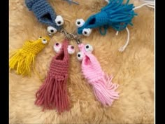 four crocheted key chains with eyes and tassels hanging from them on a furry surface