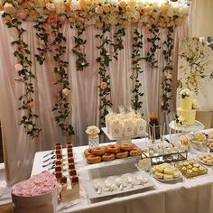 a table topped with lots of desserts next to a white wall covered in flowers