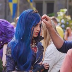 a woman with blue hair is getting her makeup done by a man in a black leather jacket