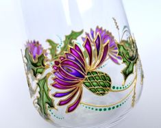 a wine glass with purple flowers painted on the outside and gold trimmings around it