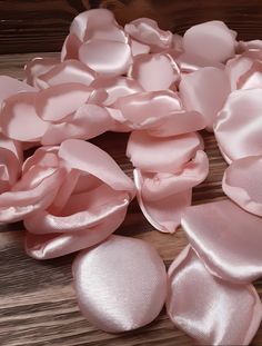 pink satin flowers are scattered on a wooden surface