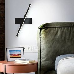 a bed with a green headboard next to a table and lamp on the wall